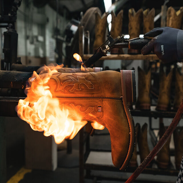 Person works on brown Double-H Western boot in factory using fire.