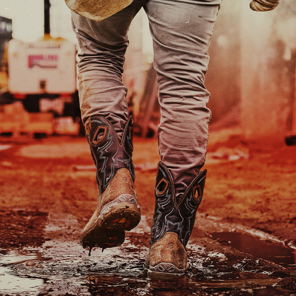 A man walking through a puddle wearing the Geddy Comp Toe in brown.