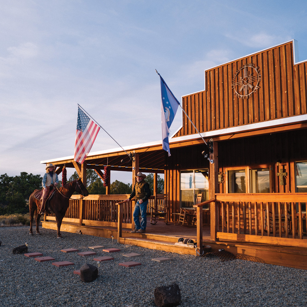 Two cowboys standing outside with a horse.