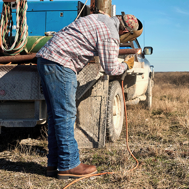A man wearing Double-H boots welding a pipe on the back of a truck.