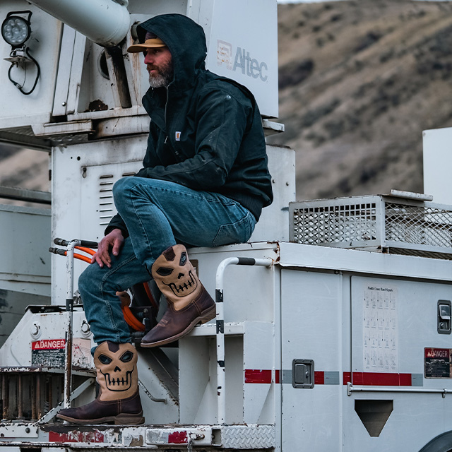 A man sitting on a truck wearing the Syphon western boots in tan.