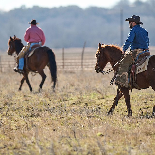 Two cowboys riding horses wearing Double-H Boots.