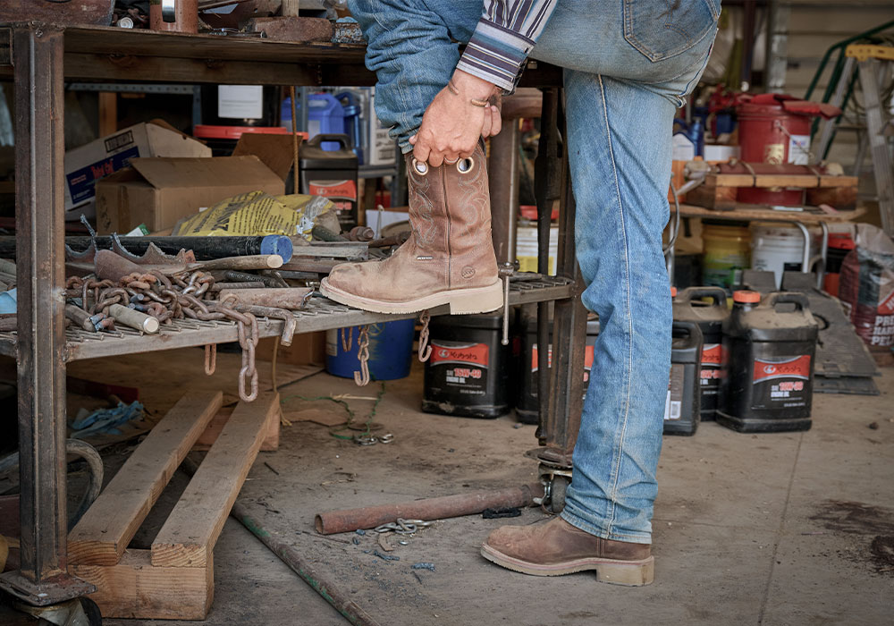 A cowboy pulling on his Roy Comp Toe western boots in brown.