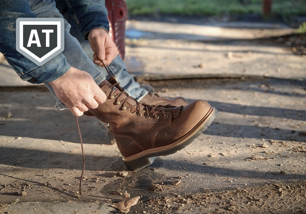 A cowboy lacing the Judge Alloy Toe western boot in brown. AT (Aluminum Toe) feature badge.